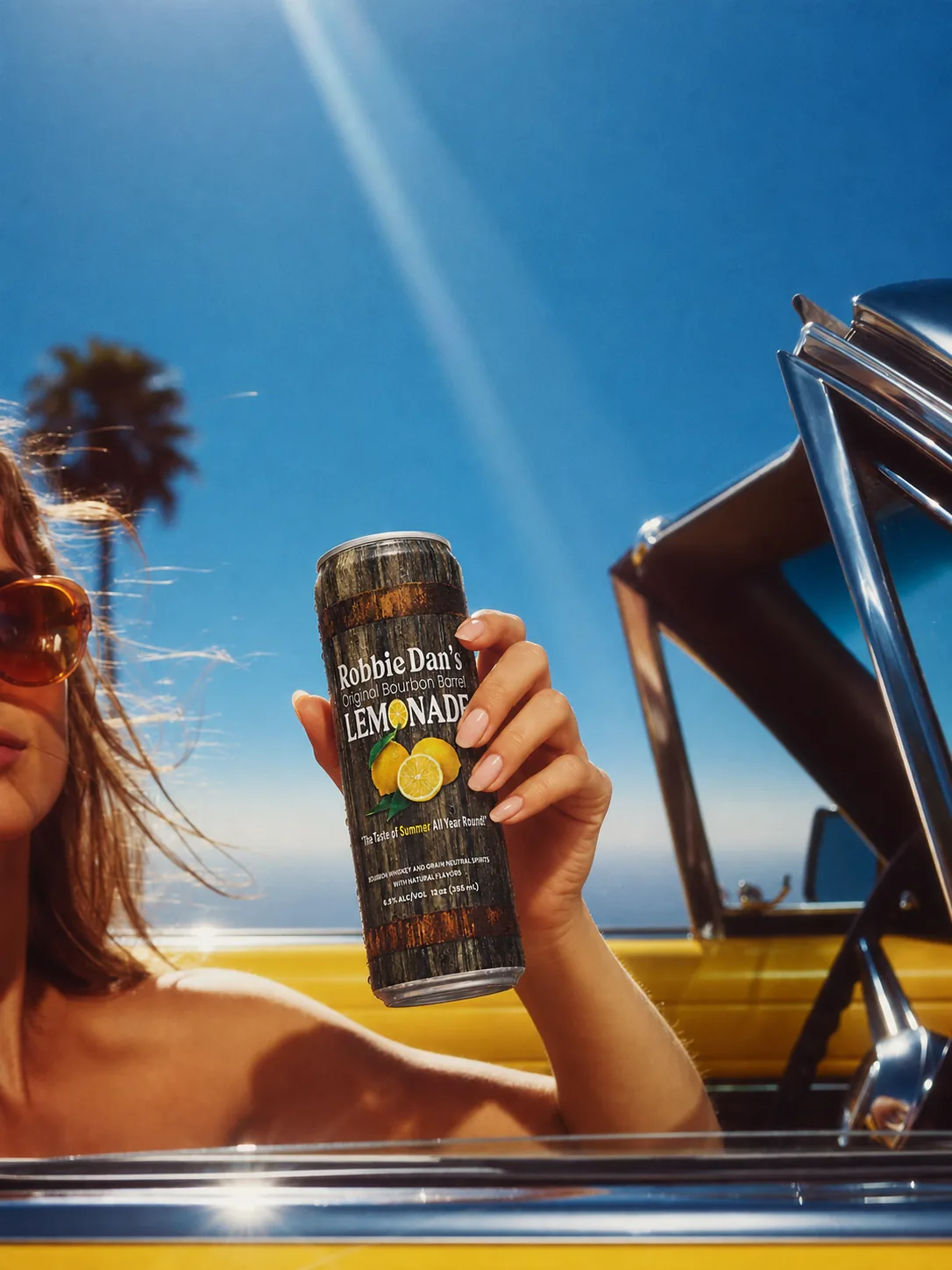 A can of Robbie Dan’s raised from a yellow convertible under blue sky.