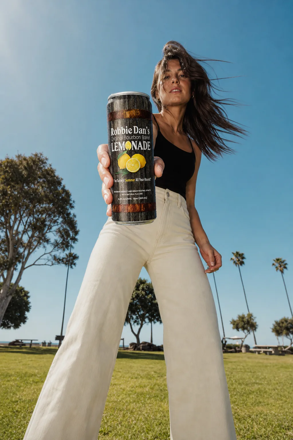 A woman holding a can of Robbie Dan’s in a sunny park.